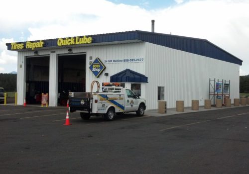 2012-08-13_13-22-38_349-1024×683 A white auto service building with signs for tires, repair, and quick lube. A white utility truck is parked outside near the entrance, and the lot is mostly empty under a cloudy sky.