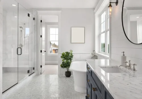 Bathrooms Bright, modern bathroom with a glass shower, freestanding tub, large windows, marble countertop, blue vanity, and a potted plant near the tub. White walls and tiled floor create a clean, airy feel.